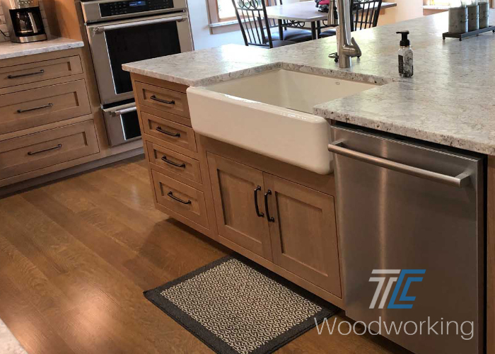 kitchen island, light brown cabinetry, white farmhouse sink, granite countertop, stainless steel dishwasher, wooden flooring