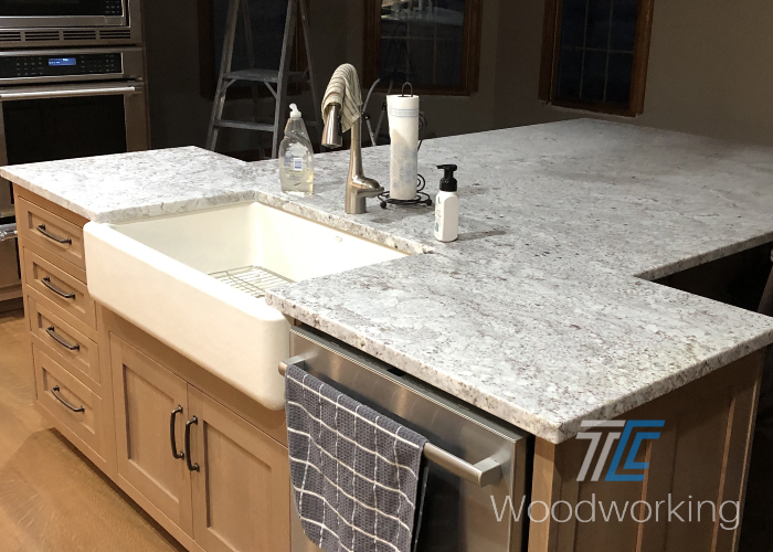 tee shaped kitchen island, large farmhouse style sink, light brown cabinet doors, marbled countertop