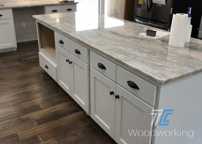 white kitchen island, marbled granite counter, black door handles,wooden flooring